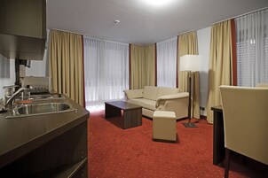 Una habitación de hotel con kitchenette, un sofá, una mesa de centro, una lámpara y una silla.