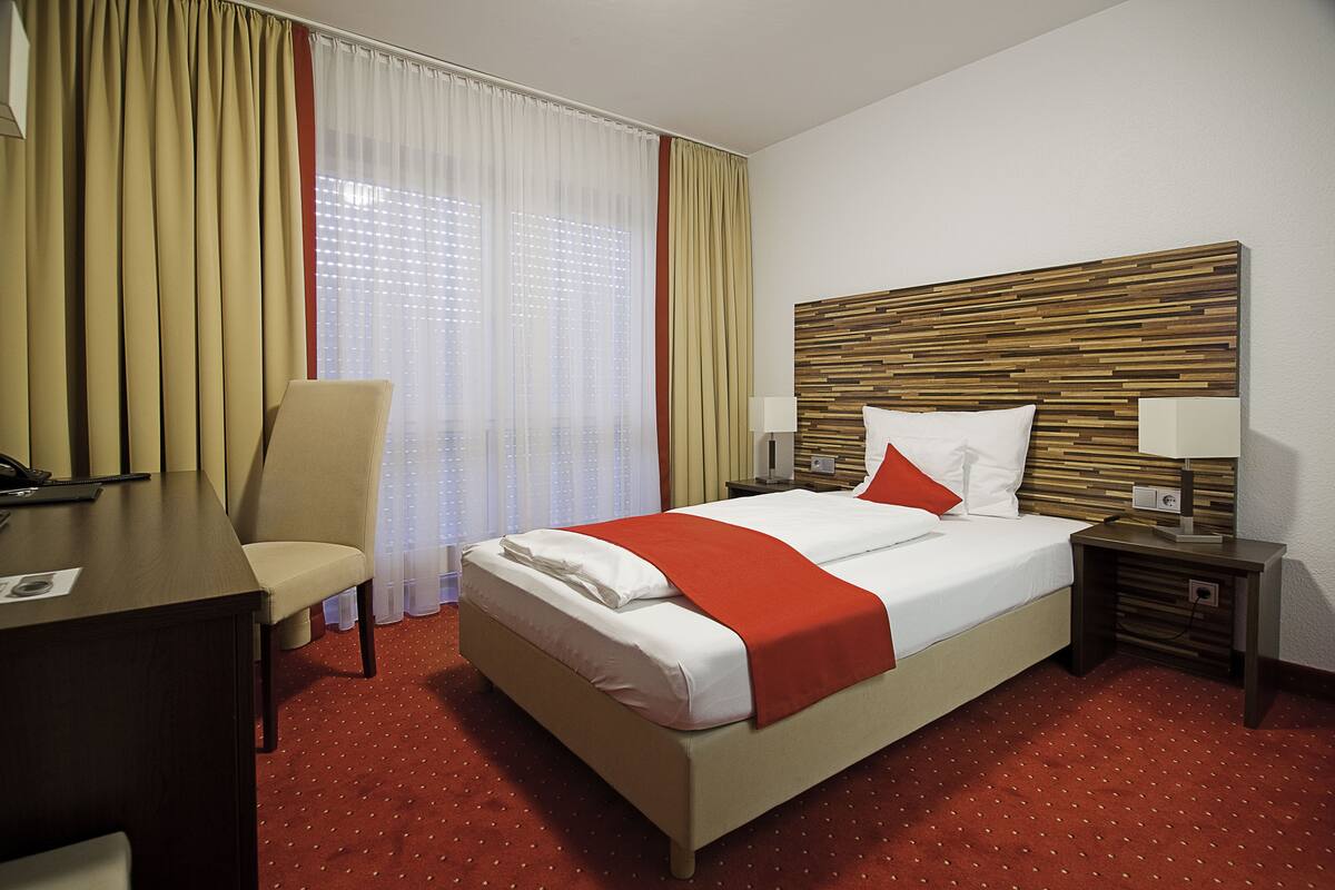 Une chambre d’hôtel avec un lit, un bureau, une chaise et une table de chevet.