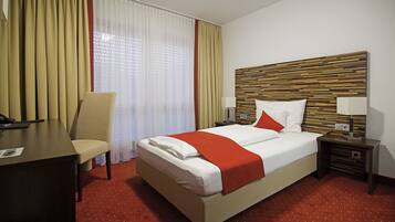 Una habitación de hotel con cama, escritorio, silla y mesita de noche.