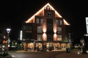 A two-story building with a brick facade and a triangular roof structure. There are multiple windows on the second floor, and the building is illuminated by exterior lights.
