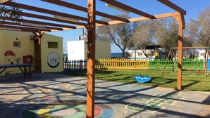 Un parque infantil con marcaciones de colores en el suelo, una pérgola de madera y un área vallada que incluye una estructura de juego con forma de barco.