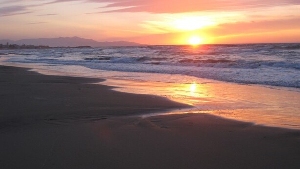 Una playa al atardecer con olas y cielo despejado.