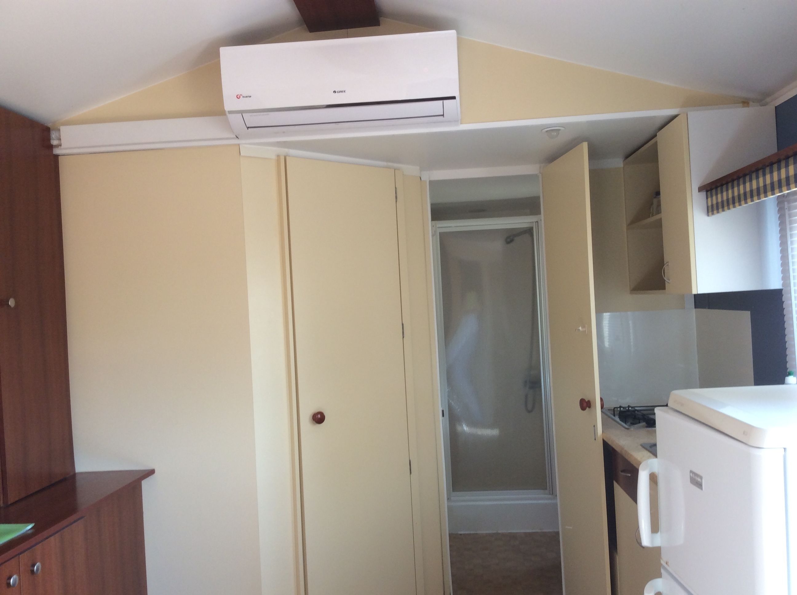 A compact kitchen with a refrigerator, an oven, and a microwave. There is a wooden cabinet and a door leading to a bathroom.