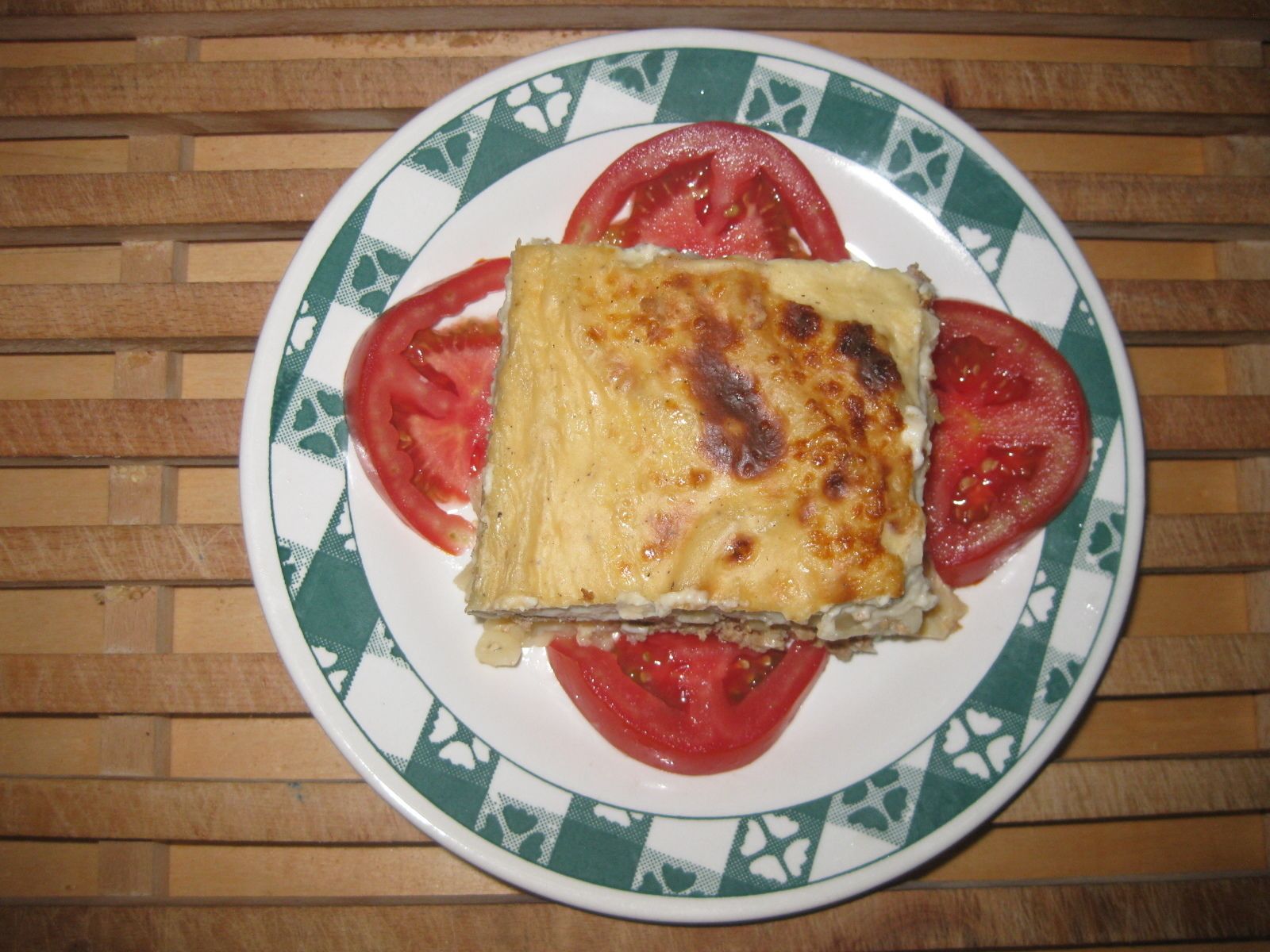 A slice of lasagna on a plate with tomato slices.