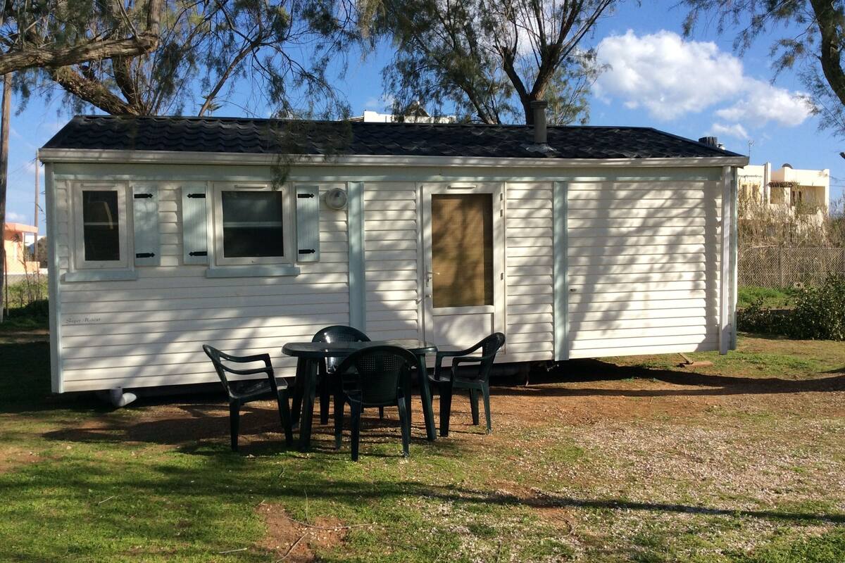 A small white mobile home with a porch, a table, and chairs.