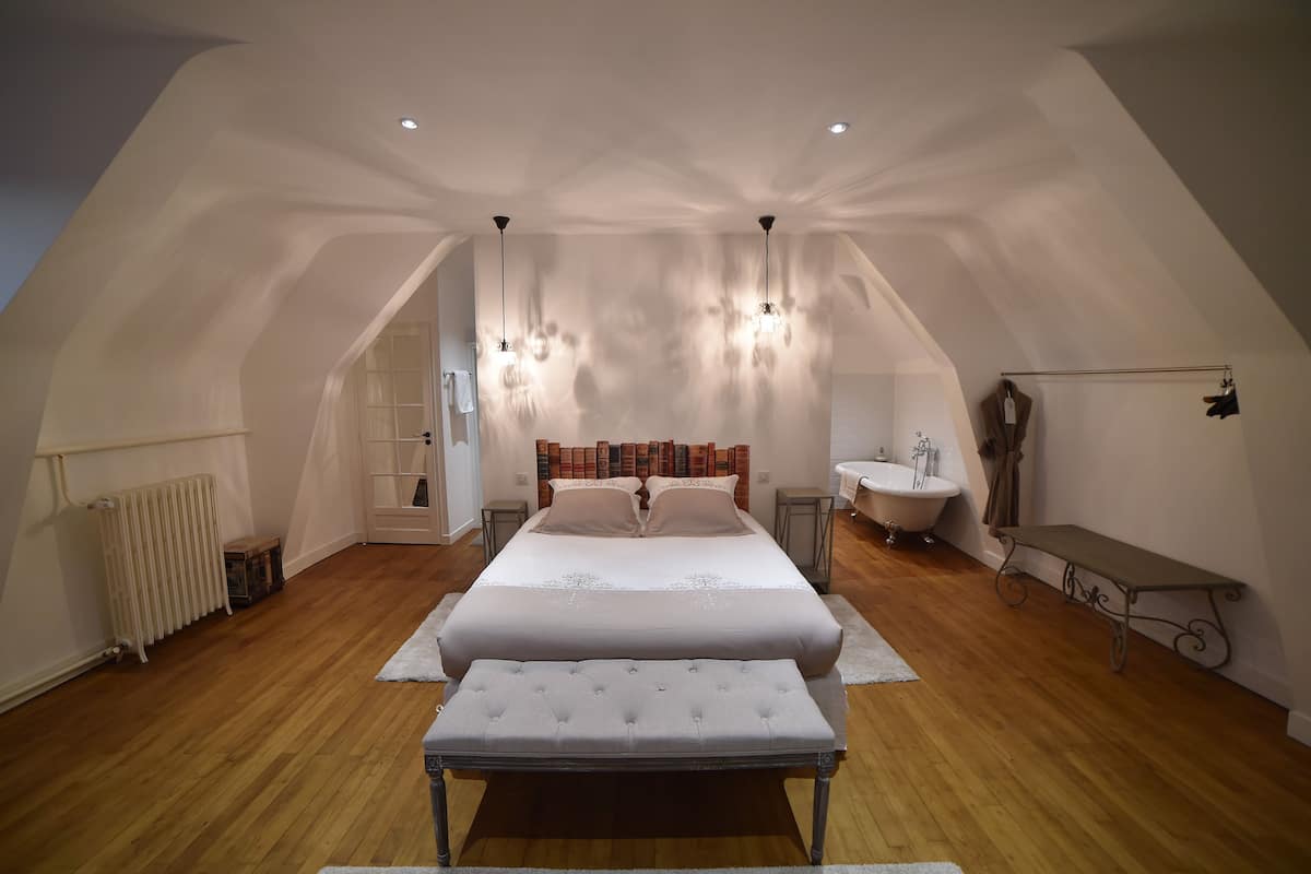 A bedroom with a large bed, a bench, a radiator, a sink, and a bench with a coat rack.