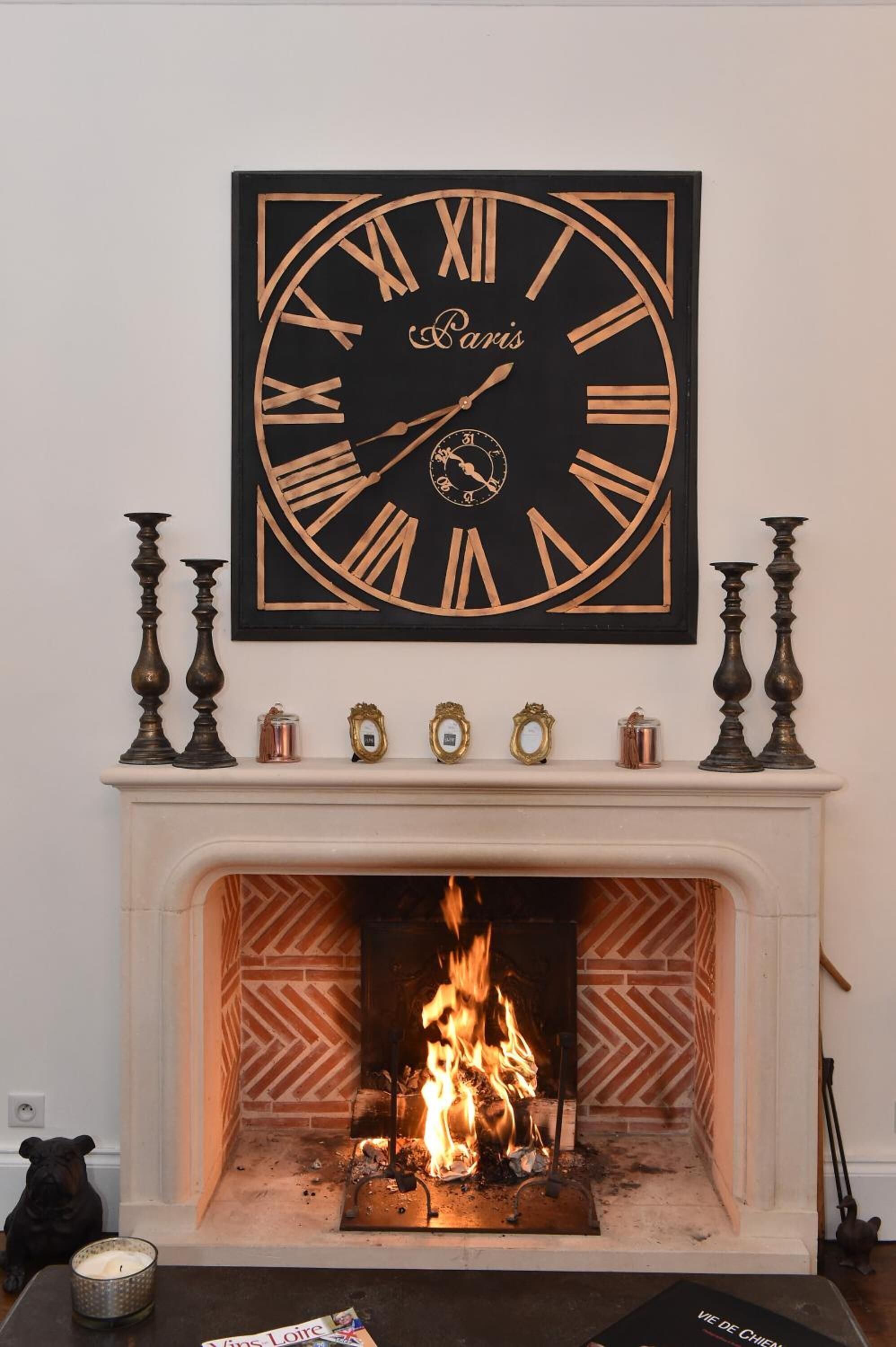 Una chimenea con un reloj grande encima, una estatua de perro y una vela en la repisa.