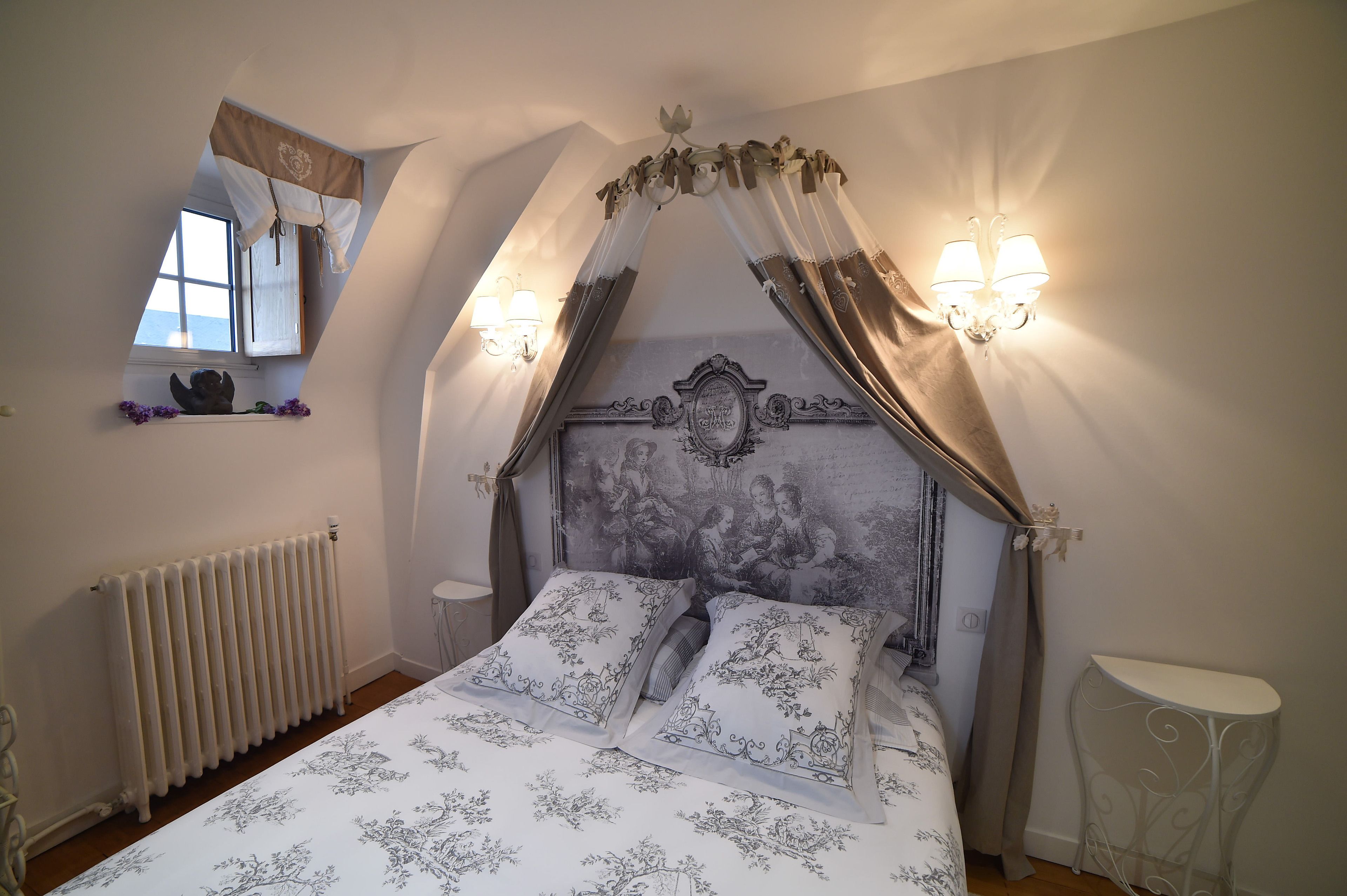 Un dormitorio con cama, ventana, radiador y mesita de noche.