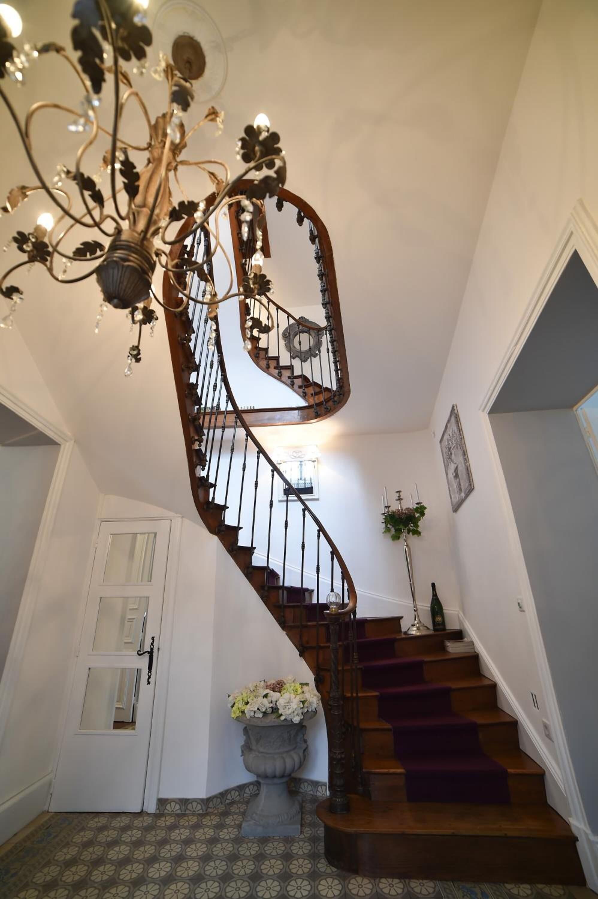Una gran escalera con un candelabro, una planta en maceta y una puerta al final.