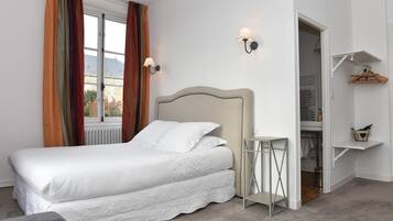 A neatly arranged bedroom with a bed, a small table, and a closet with hanging clothes.