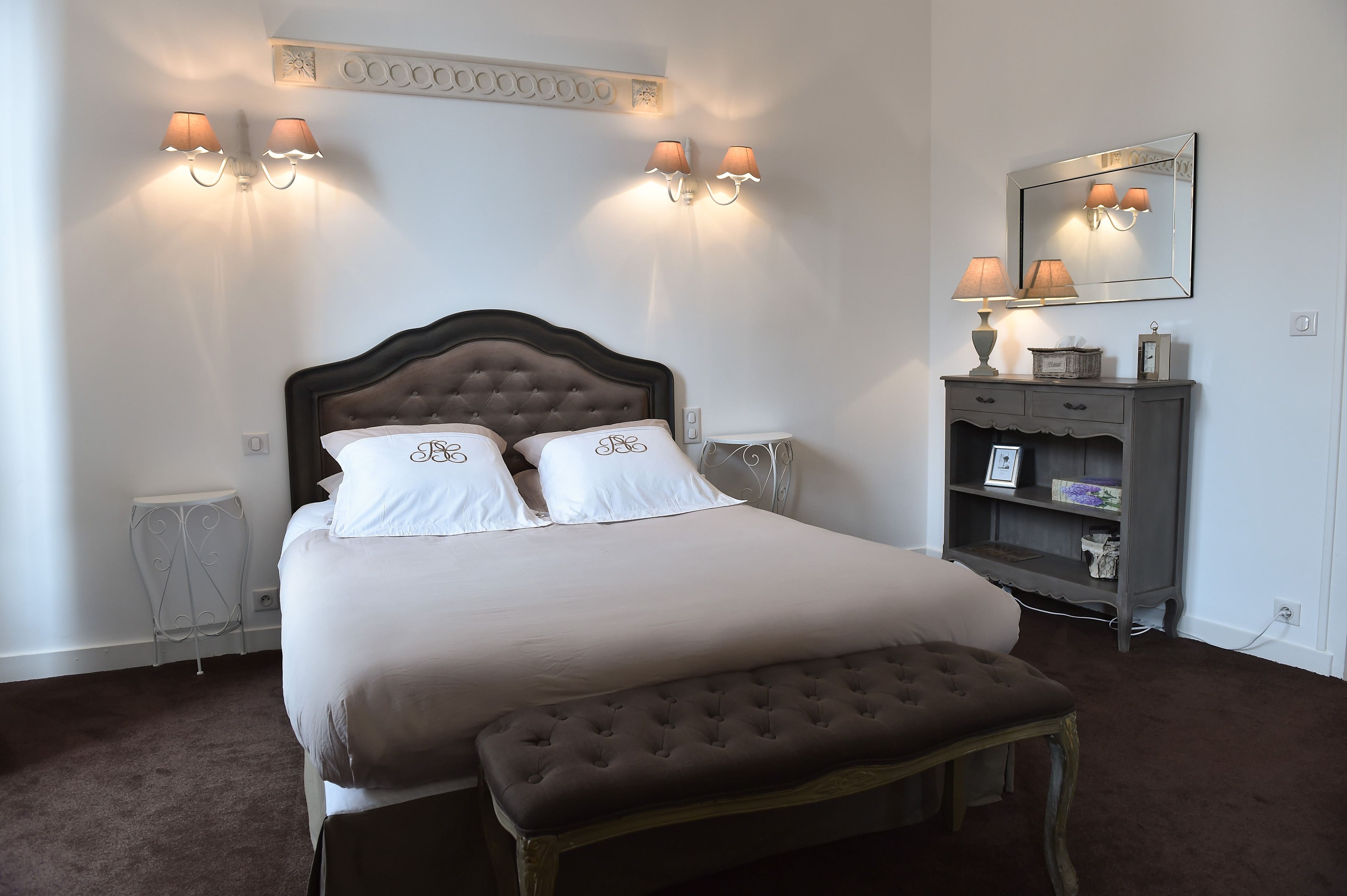 A neatly arranged bedroom with a large bed, bedside lamps, a dresser, and a mirror.