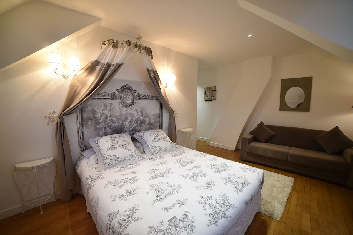 A bedroom with a canopy bed, a brown sofa, and a small round table.