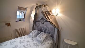 A bedroom with a bed, a nightstand, a wall-mounted lamp, a radiator, and a window with curtains.