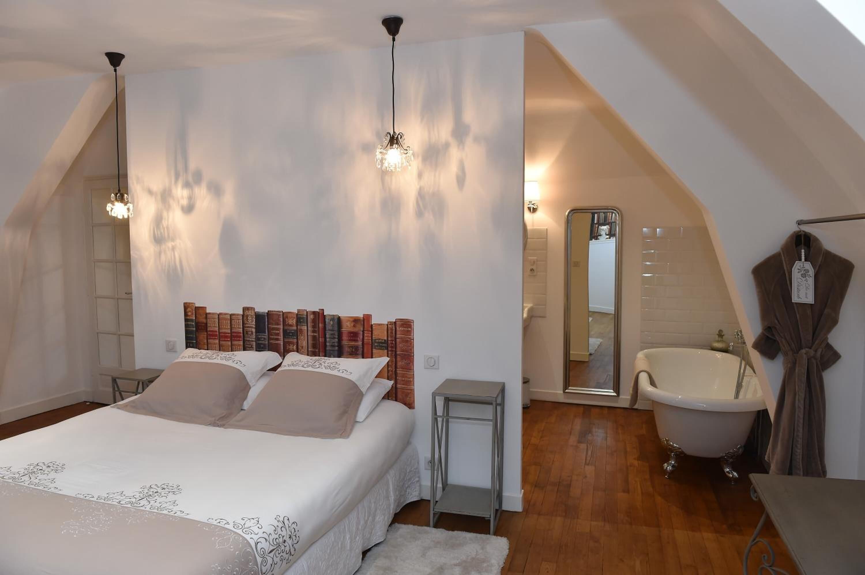 A bedroom with a large bed, a vanity with a mirror, a bathtub, and a small table.