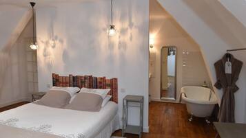 A bedroom with a large bed, a vanity with a mirror, a bathtub, and a small table.
