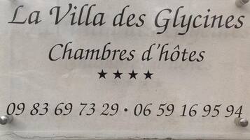 Señal de 'La Villa des Glycines' con la dirección '09 83 69 73 29 · 06 59 16 95 94' y tres estrellas que indican la calificación del hotel.