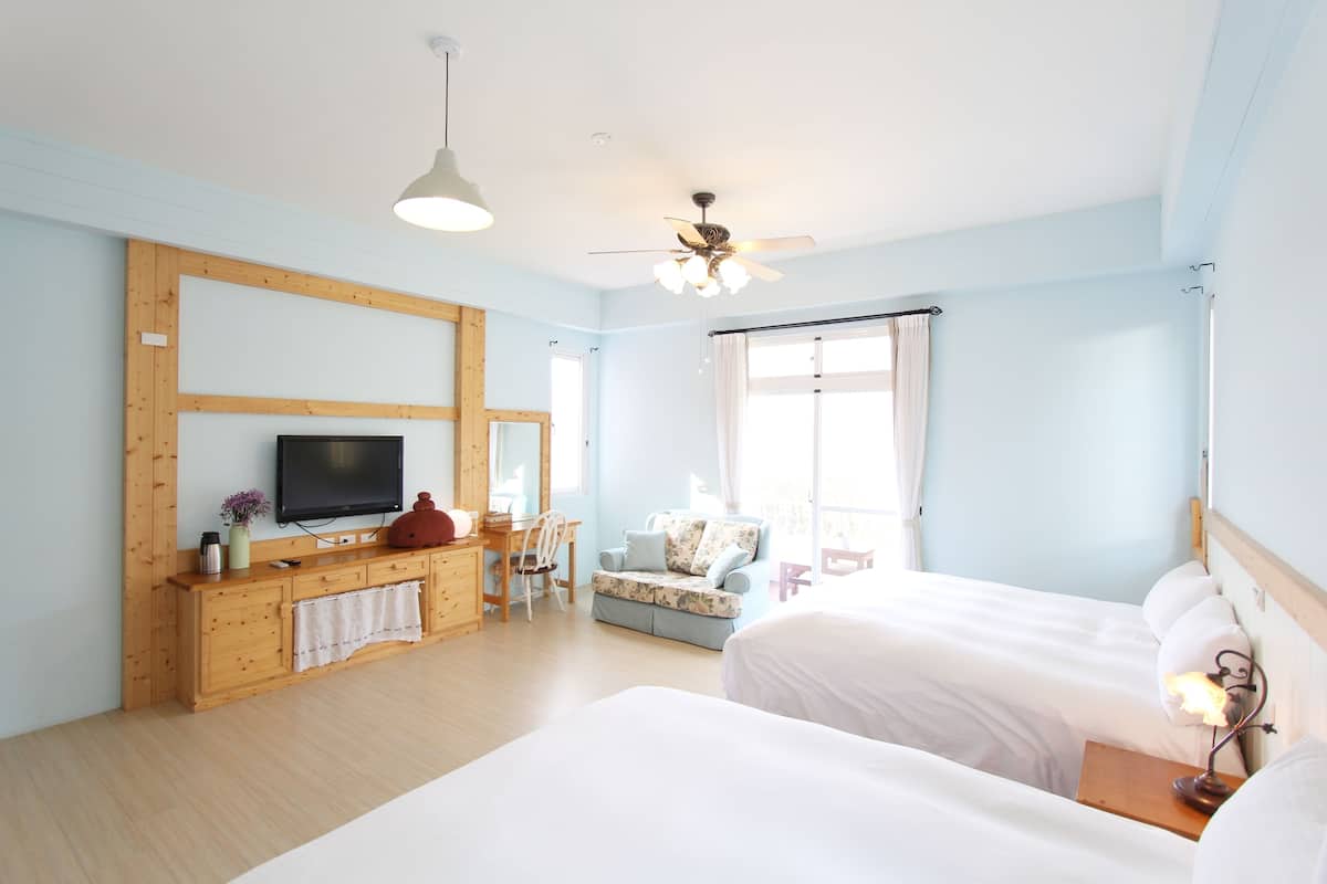 A hotel room with two beds, a TV, a wooden desk, a chair, and a balcony with a view.