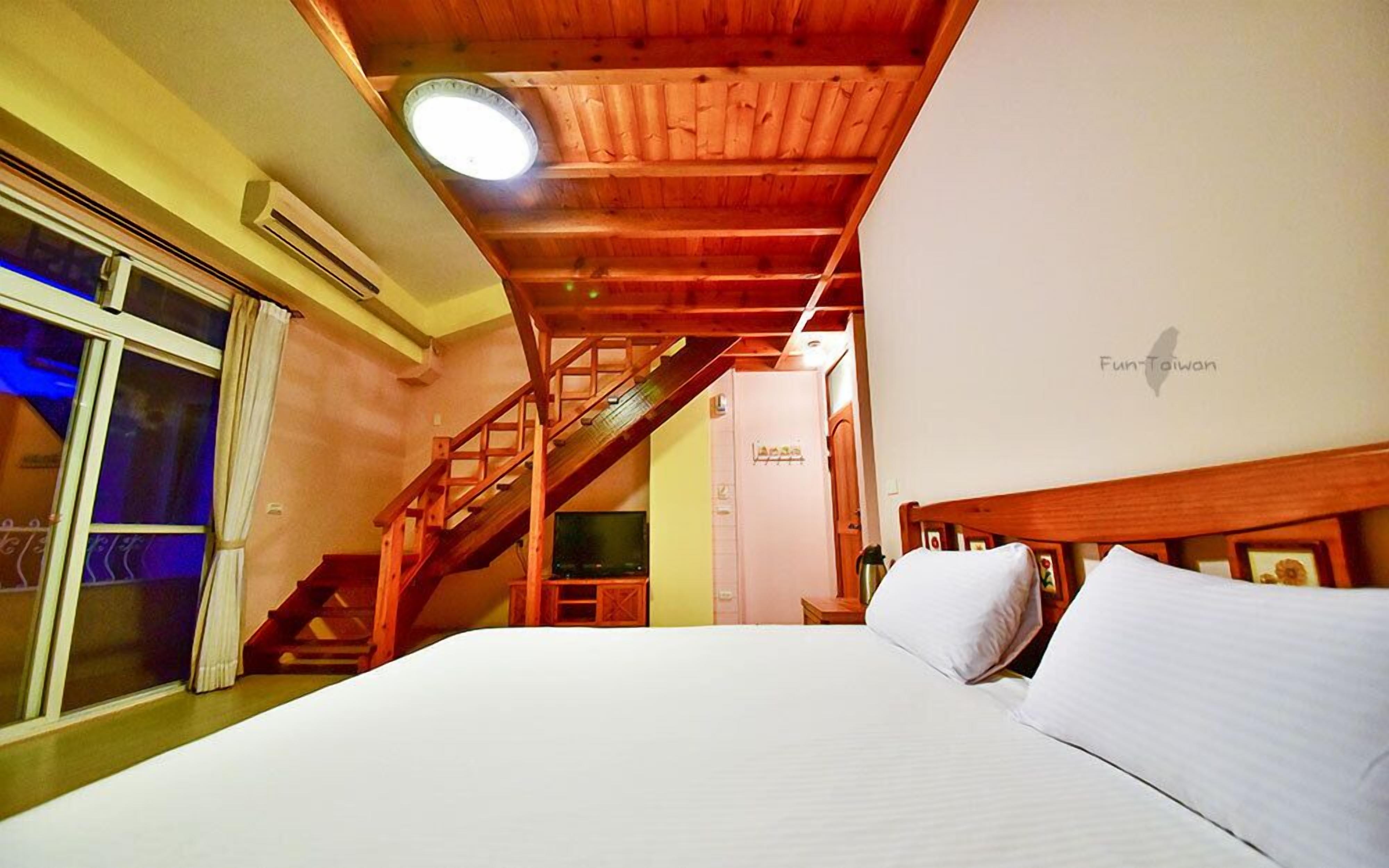 A bedroom with a wooden staircase, a bed with white bedding, and a ceiling light.
