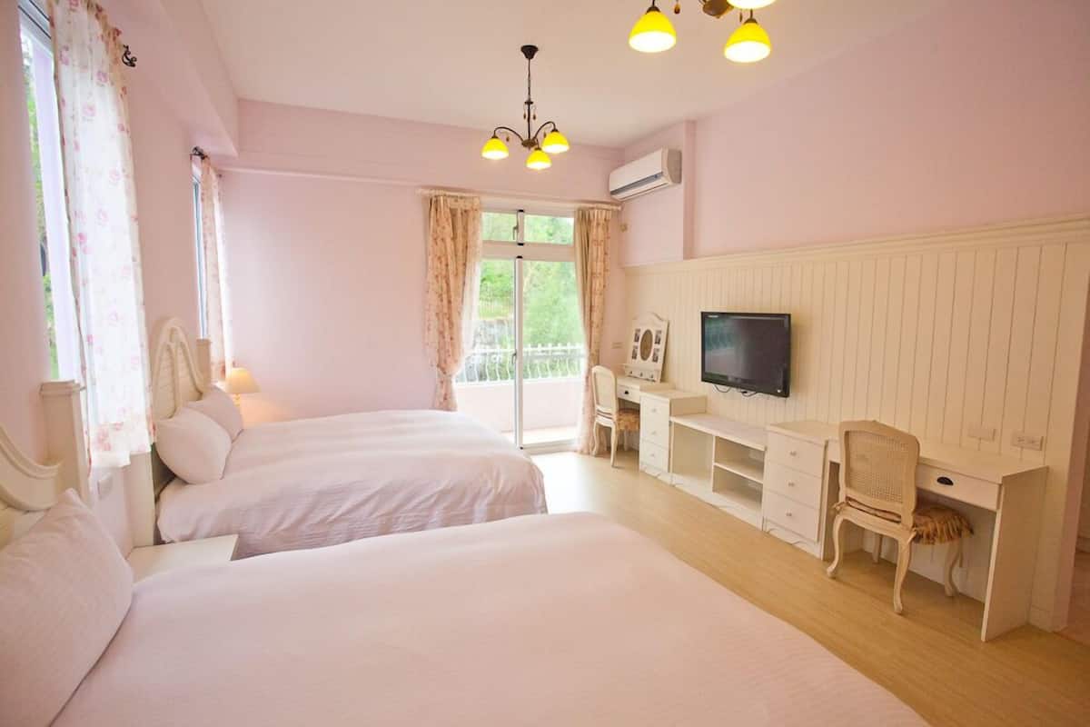 A hotel room with two beds, a desk with a chair, a television, and a large window with curtains.