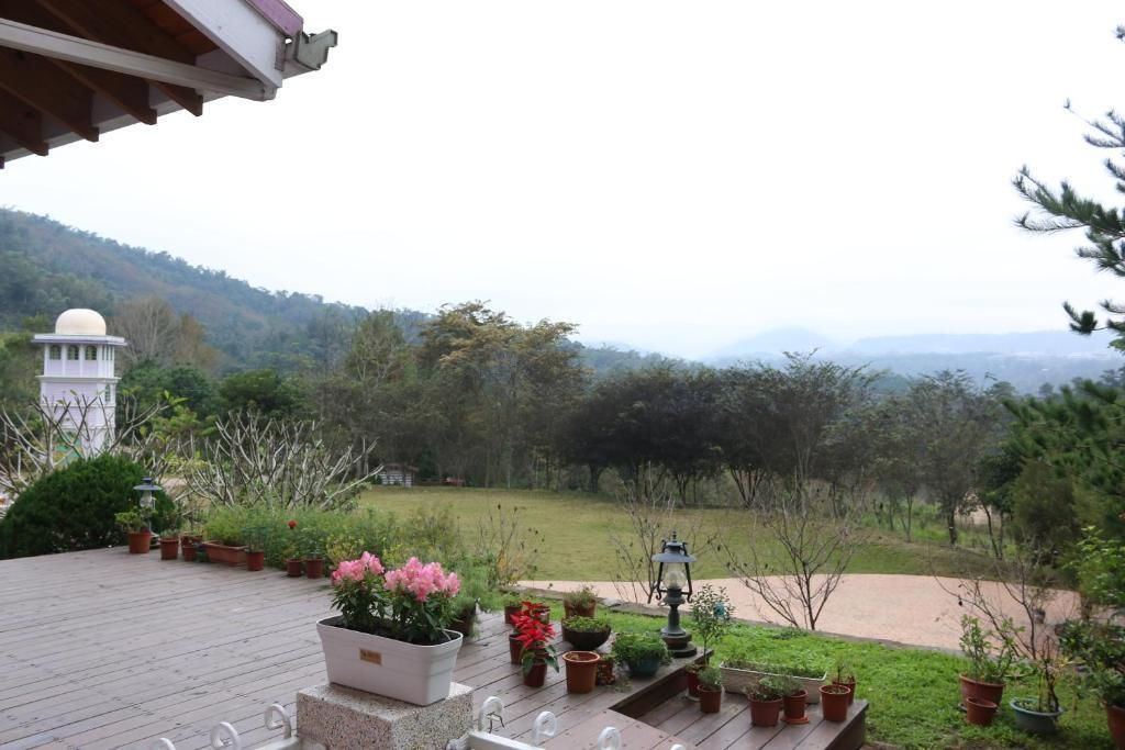 Une terrasse agrémentée de plantes en pot et d’une lanterne, d’où l’on peut admirer un jardin luxuriant et des collines lointaines.