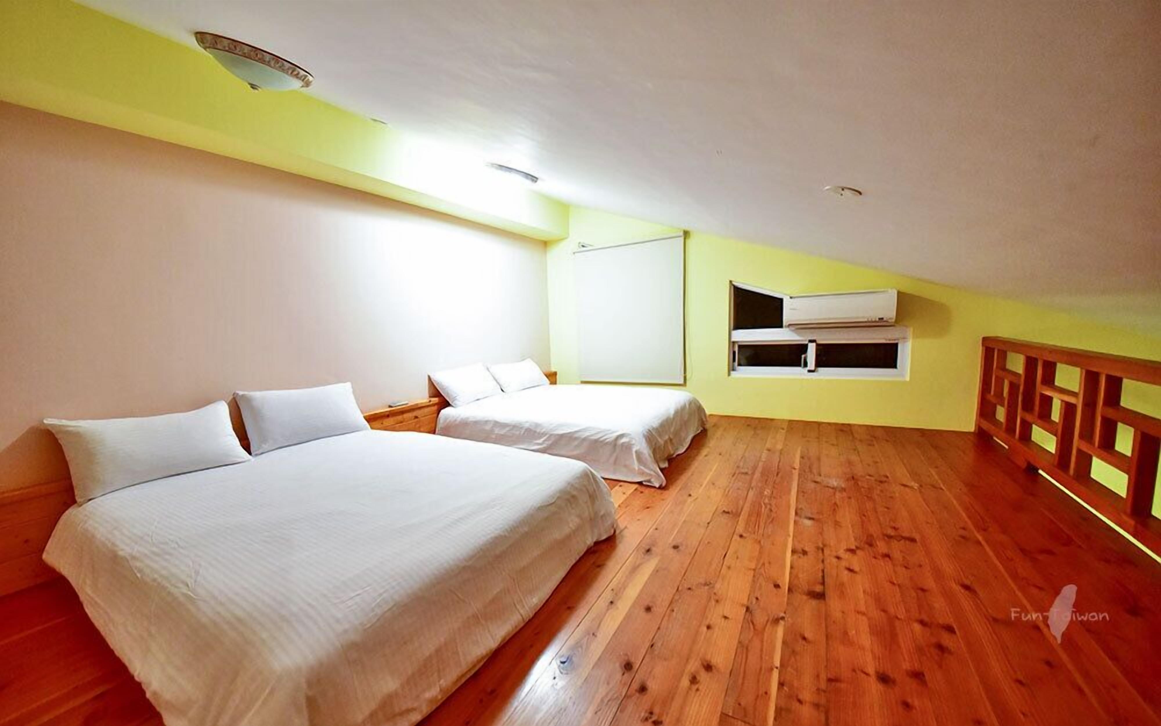 A room with two beds, wooden flooring, a white ceiling, and a yellow wall.