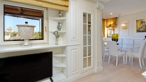 A dining area with a white table and chairs, a window with a view of a dome, and a TV on a stand. - Rione Trastevere apartment (Rome)