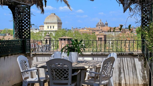 A terrace with a table and chairs, a potted plant, and a view of historic buildings. - Rione Trastevere apartment (Rome)