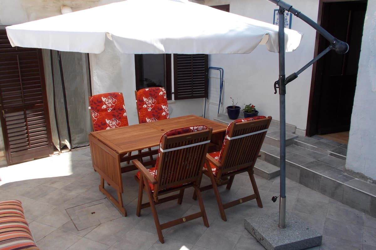 Eine Terrasse im Freien mit einem Holztisch, Stühlen, einem weißen Sonnenschirm und einem Metalllaternenpfahl.