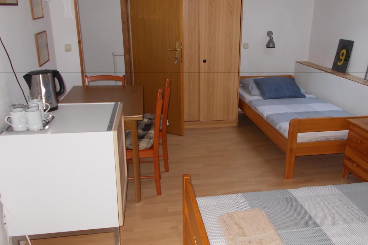 Ein kleines Zimmer mit einem Bett, einem Schreibtisch, einem Stuhl und einer Kommode.