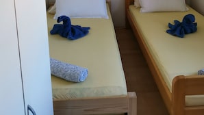 Deux lits simples avec une literie blanche et beige, une armoire en bois et un appareil de climatisation fixé au mur.