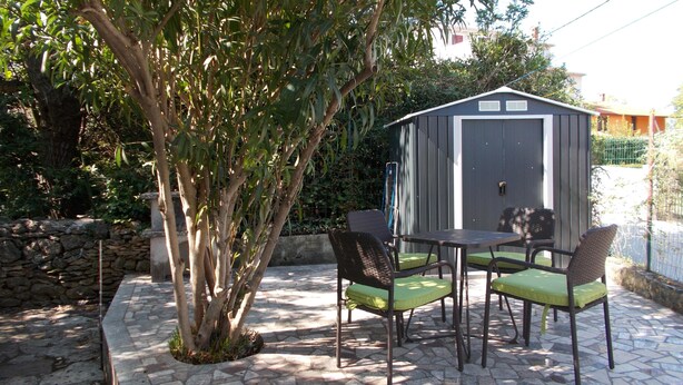 Une terrasse extérieure avec une table et des chaises, un abri de jardin et un arbre.