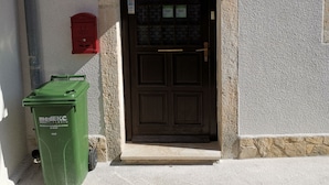 Une entrée d’immeuble avec une porte marron foncé, une boîte aux lettres rouge et une poubelle verte portant l’inscription « medEKE ».
