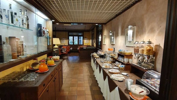 Een lange buffetlijn met verschillende gerechten en dranken, een betegelde vloer en een plafond met ruitmotief.