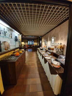 Een lange buffetlijn met verschillende gerechten en dranken, een betegelde vloer en een plafond met ruitmotief.