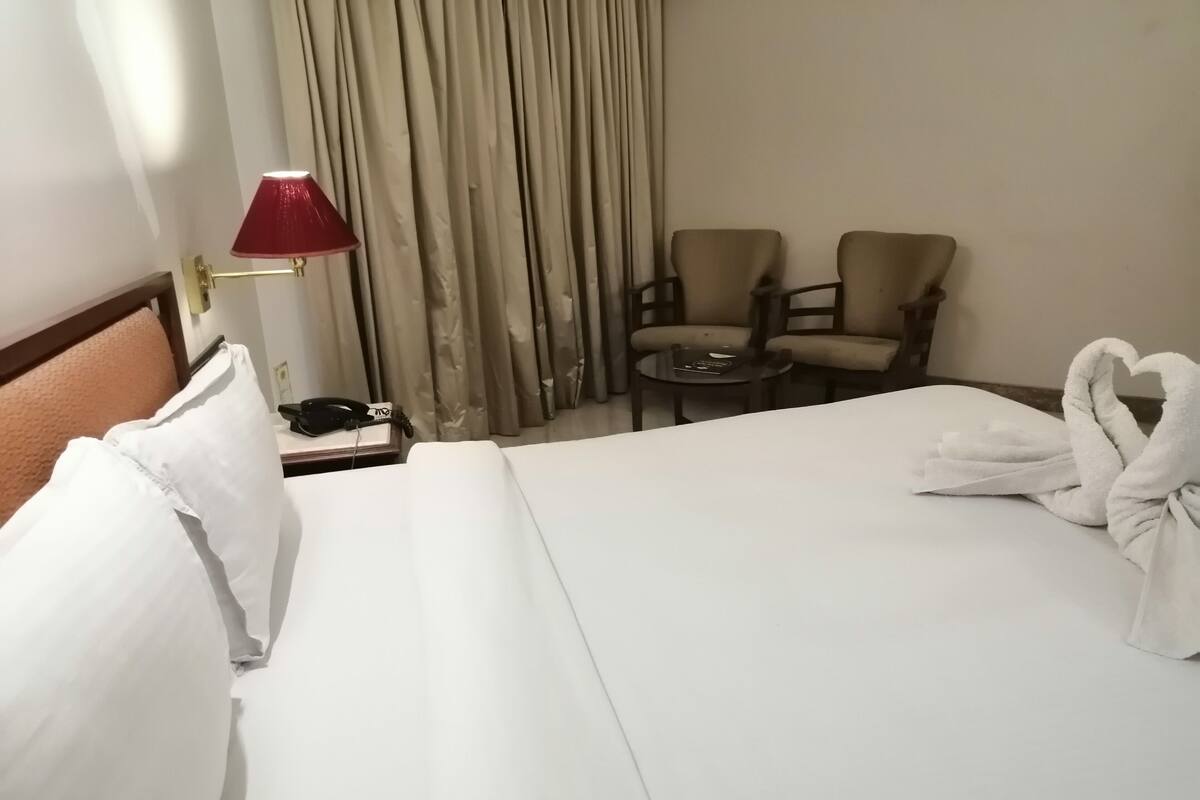 A hotel room with a neatly made bed, a bedside lamp, a telephone, two chairs, and a table.