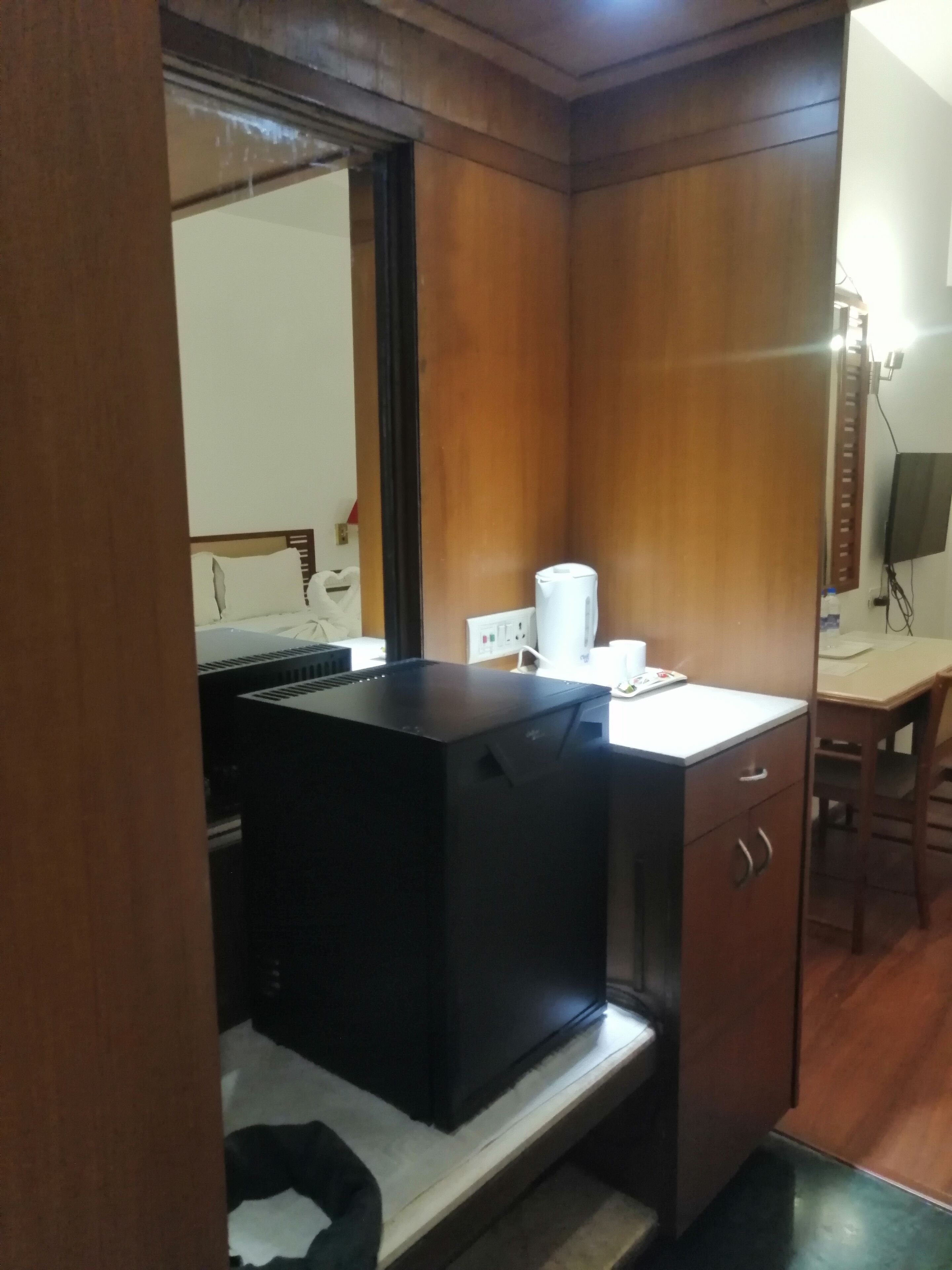 Una habitación pequeña con una cama, un escritorio, un calentador negro, una taza blanca y un espejo.