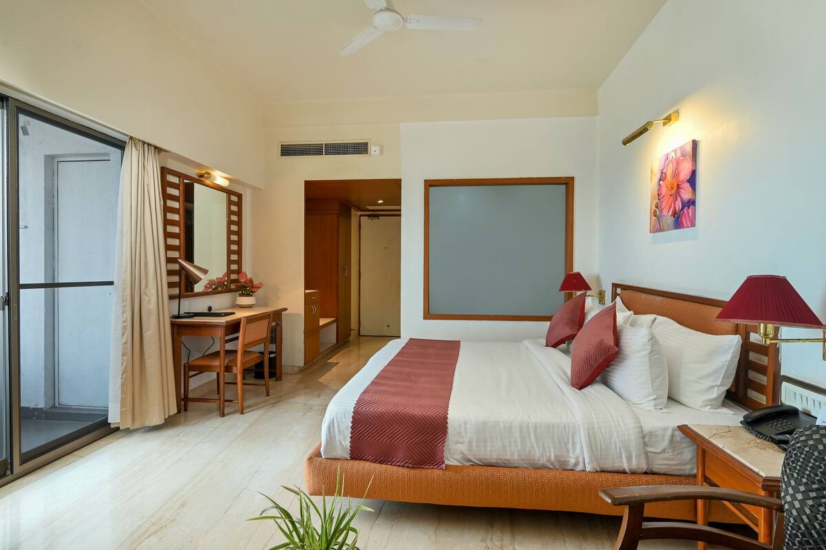 A hotel room with a bed, desk, chair, and a view of the outside.