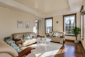 A spacious living room with two beige sofas, a white coffee table, and large windows providing natural light.