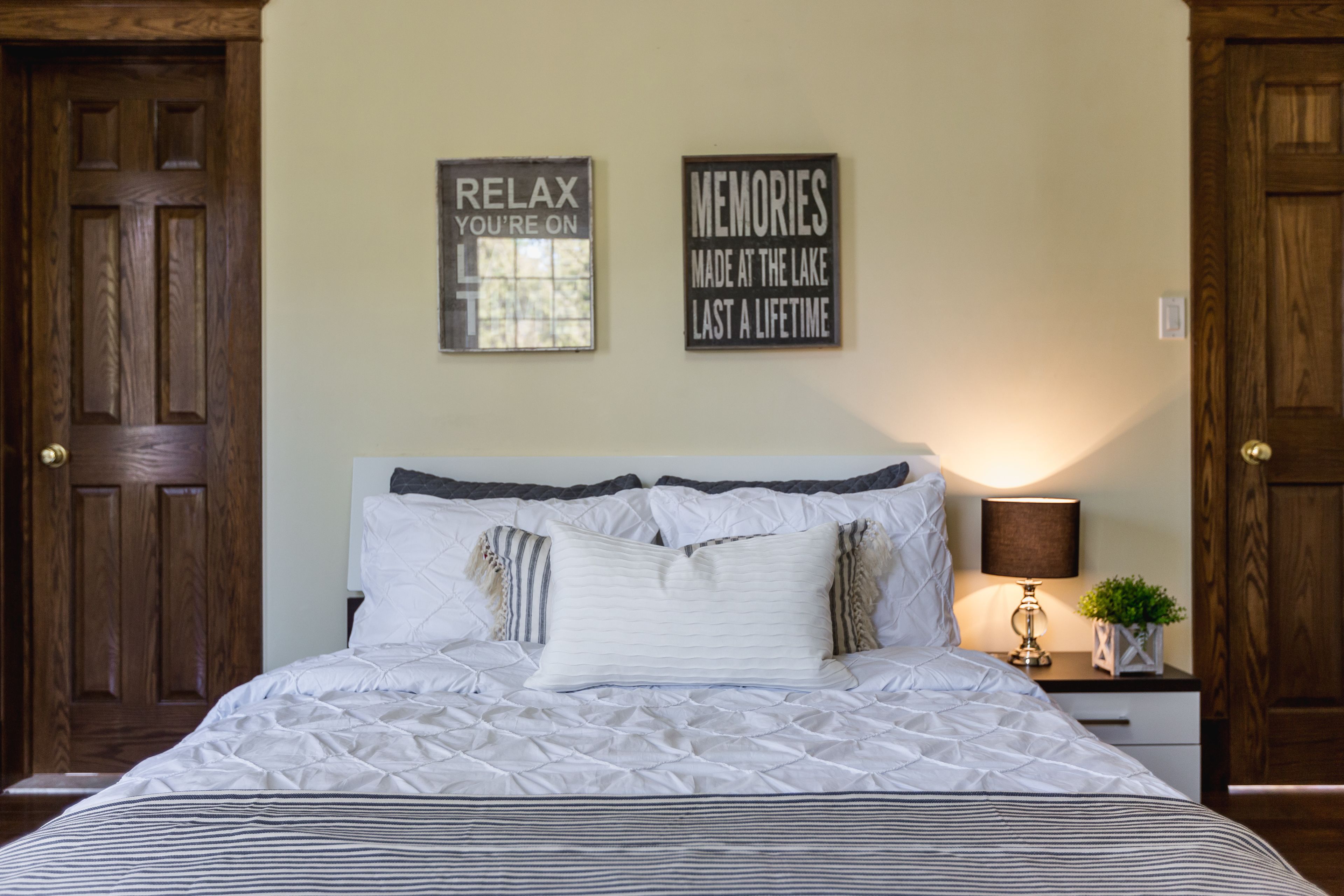 A bedroom with a bed, two wooden doors, a nightstand with a lamp, and two wall-mounted signs.