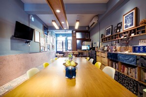 A conference room with a long table, chairs, a TV, and shelves with books and decorative items.
