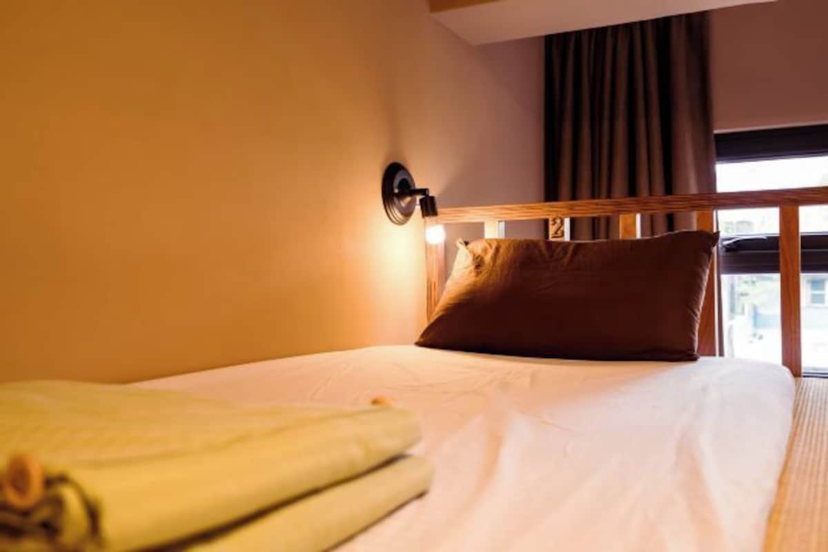 A hotel room with a bed, a nightstand, a lamp, and a window with curtains.