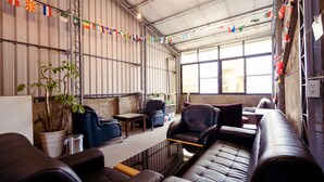 Ein geräumiger Lounge-Bereich mit Ledersofas, einem Couchtisch und Topfpflanzen. Flaggen sind an der Decke befestigt, und der Raum verfügt über große Fenster.