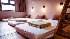 Ein Zimmer mit drei Betten, Holzböden und einem fensterbepflanzten Fenster.