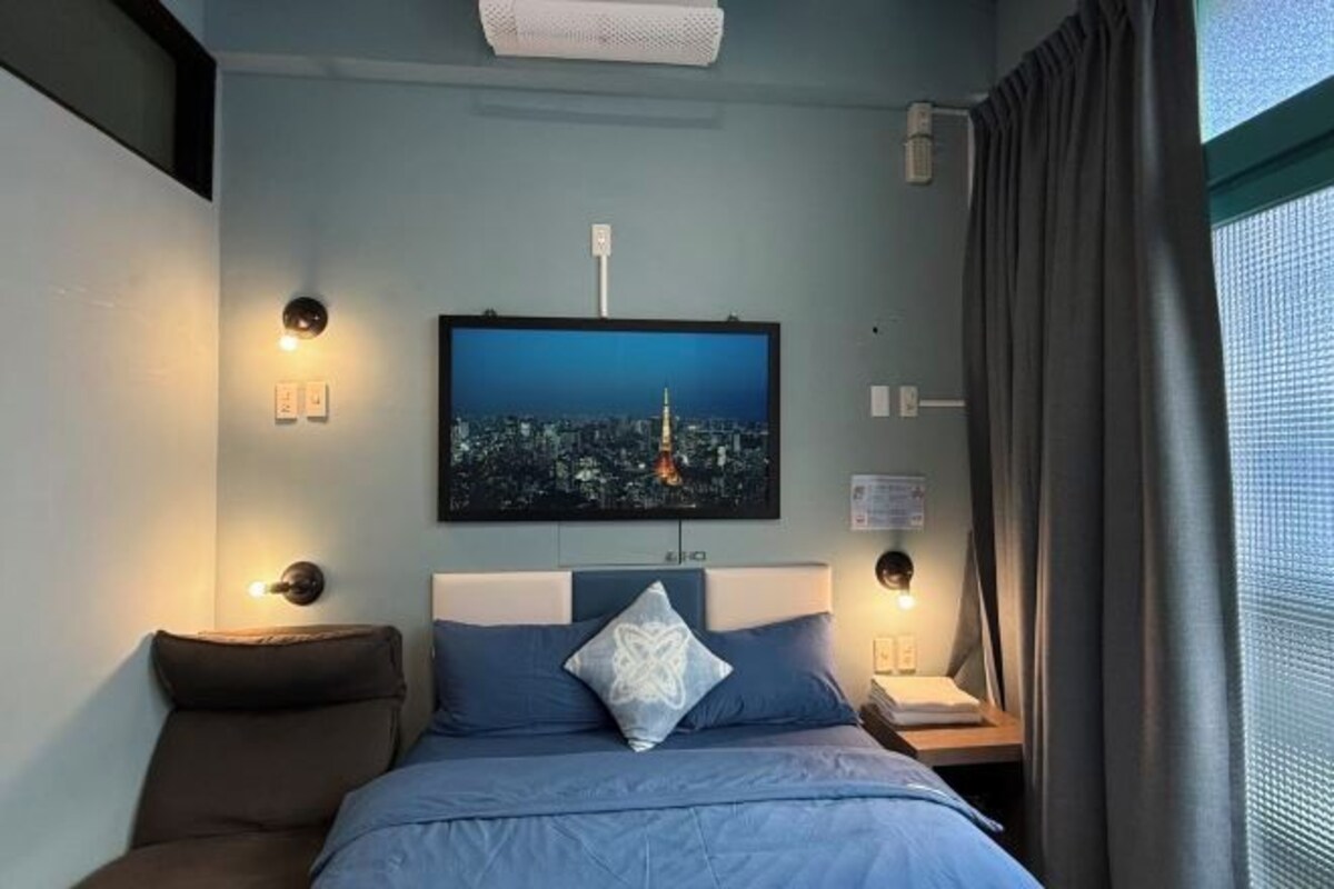 A hotel room with a bed, a nightstand, a wall-mounted TV, and a window with curtains.