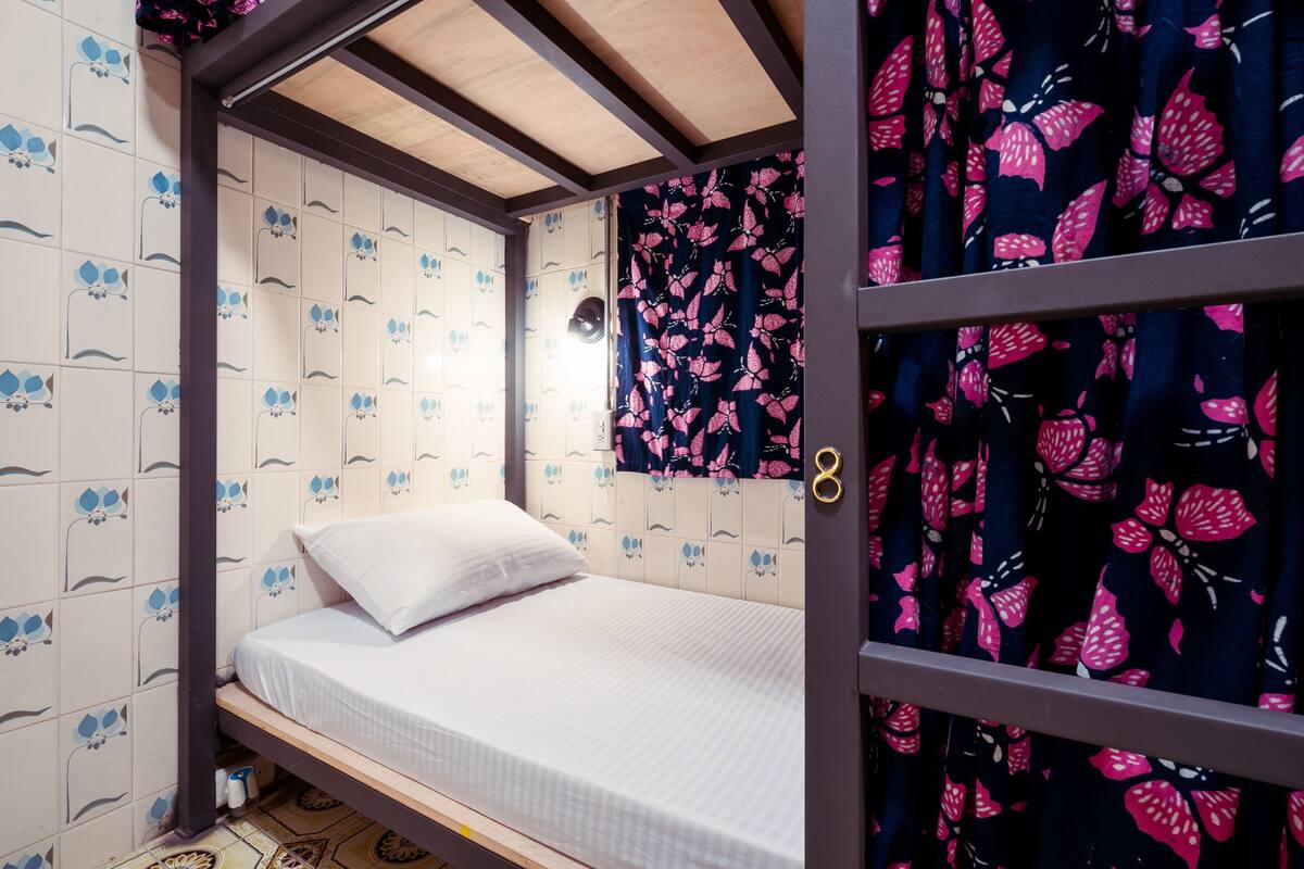 A single bed in a room with patterned walls and a curtain with a floral design.