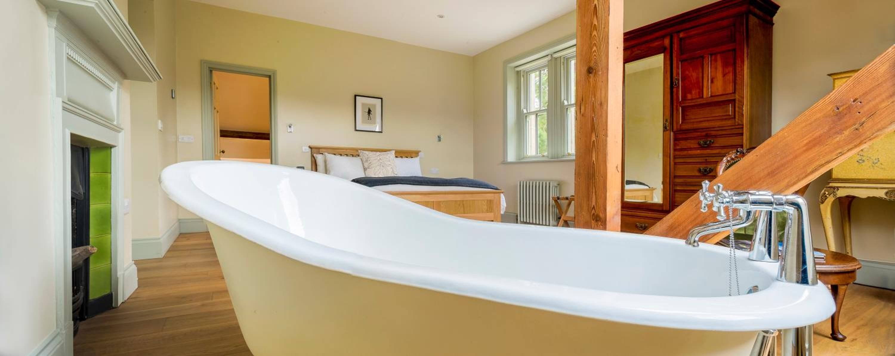 A room with a large freestanding bathtub, a wooden cabinet, and a bed with a headboard.
