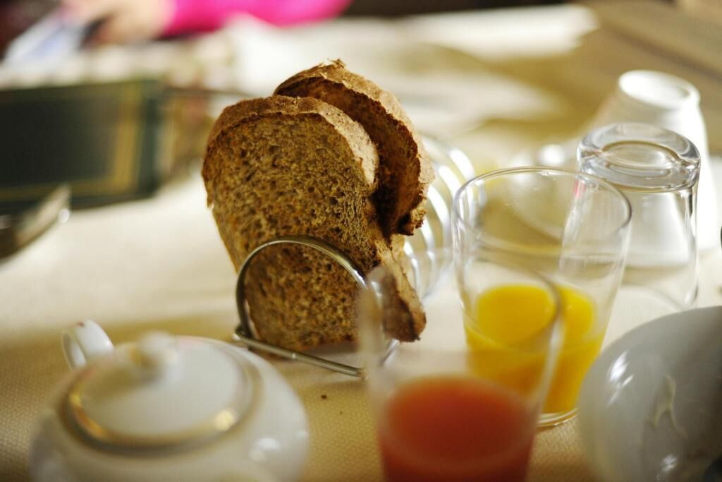 Ein Frühstückstisch mit Brot, einem Glas Orangensaft und einem Teekännchen.