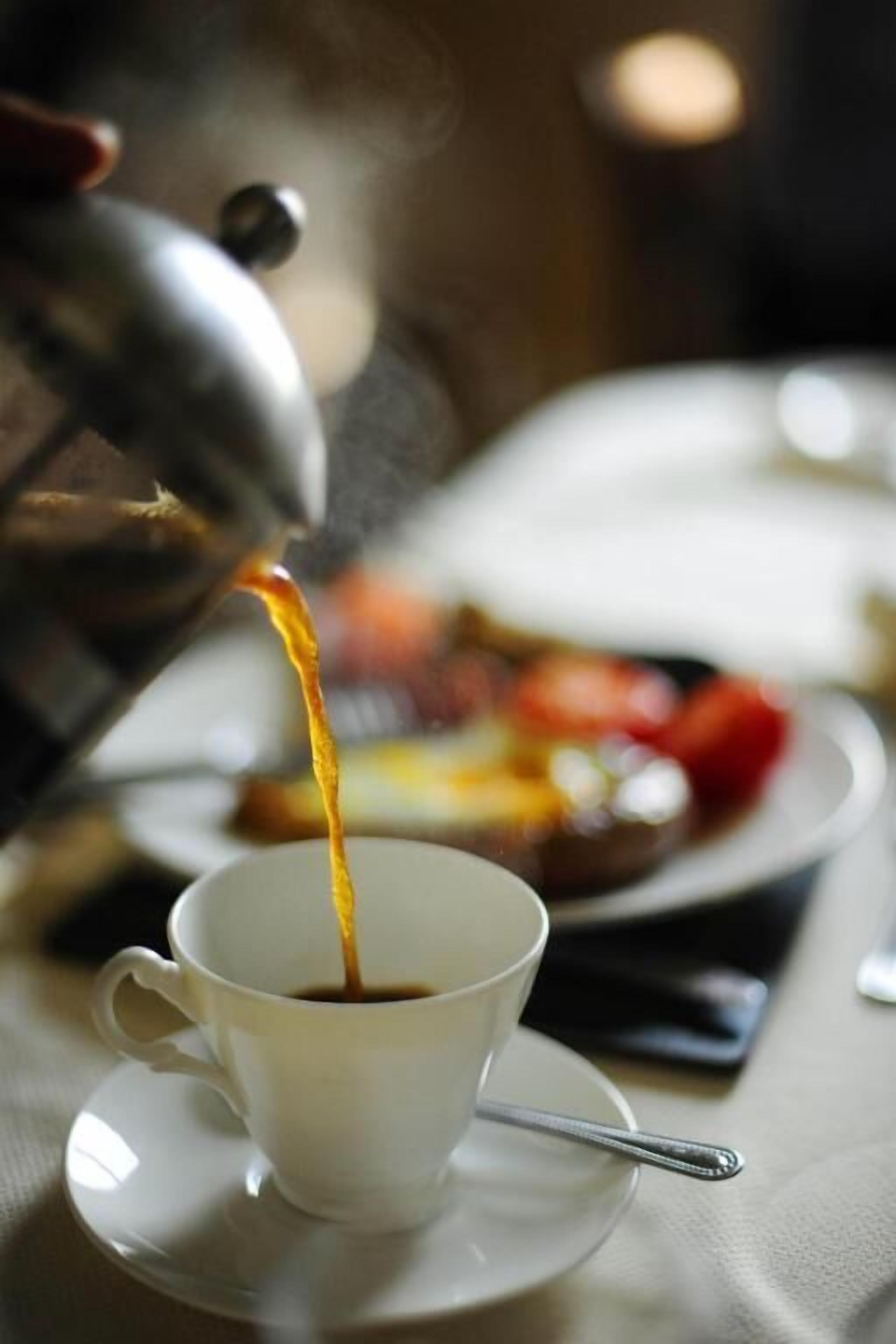 A cup of coffee being poured from a metal pot.