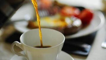 A cup of coffee being poured from a metal pot.
