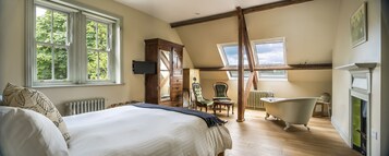Un dormitorio con una cama grande, un armario de madera, un sillón verde, una bañera de patas de león y un tragaluz.